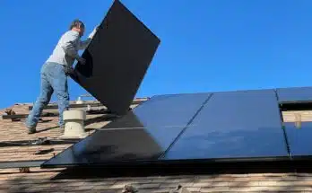 un homme installe des panneaux solaires sur le toit d'une maison