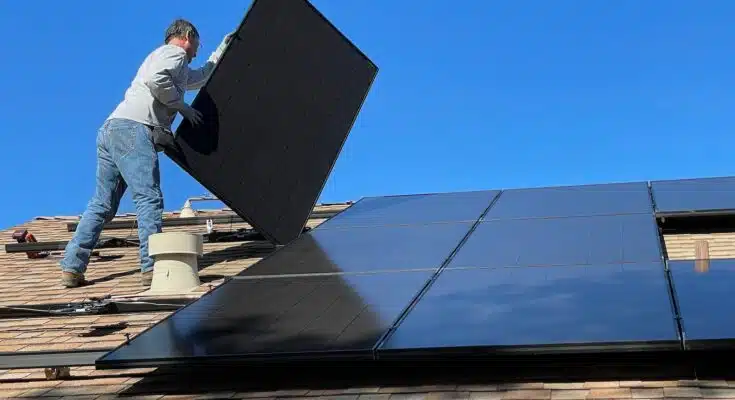 un homme installe des panneaux solaires sur le toit d'une maison
